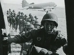 Photo of soldiers with lots of gear and parachutes walking onto a plane