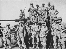 Photo of a large group of soldiers in uniform sat and stood on a tank and in front of it