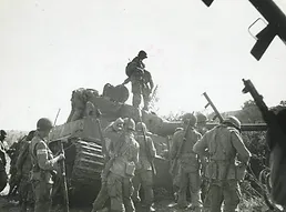 Photo of soldiers with rifles stood in front of a tank and on top of it