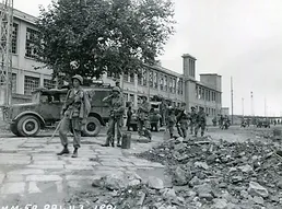 Photo of soldiers by a large building and a truck they are carrying equipment