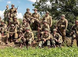 Soldiers in a group with full uniform and rifles some stood slightly higher on a small hill